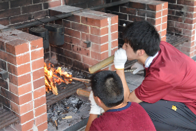 写真：飯盒炊さんの火加減を調節する大学生と小学生