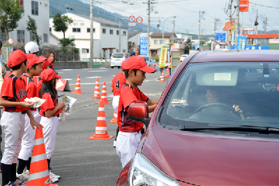 写真：ドライバーにお守りなどを手渡す野球チームの子ども