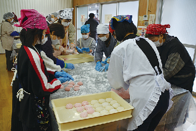 写真：つきたてのお餅をお母さんたちと一緒に丸める小学生