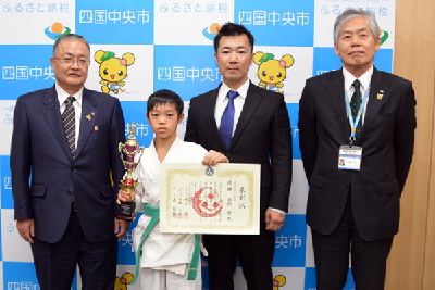 写真：賞状とトロフィーを持った奥村くんと篠原市長らの記念写真